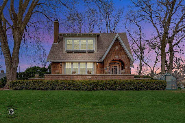 english style home featuring an exterior structure, a chimney, brick siding, a front yard, and an outdoor structure