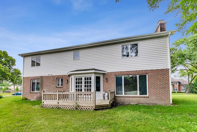 back of house featuring a lawn, brick siding, a chimney, and a deck