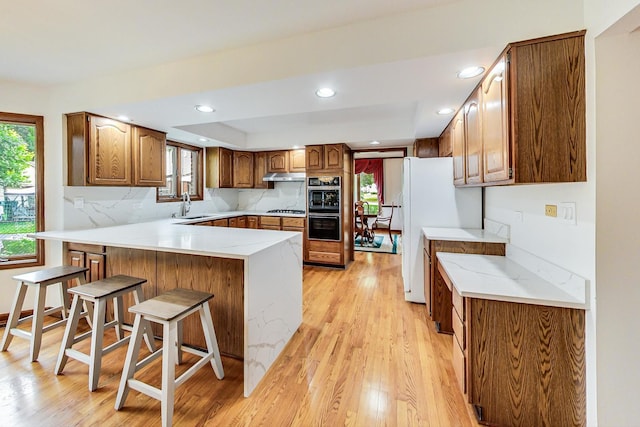 kitchen with a peninsula, light wood finished floors, under cabinet range hood, a sink, and a kitchen breakfast bar