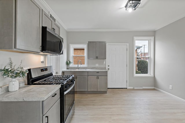 kitchen featuring light countertops, ornamental molding, light wood-type flooring, stainless steel gas stove, and gray cabinets