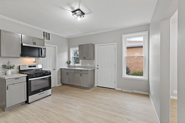 kitchen with light countertops, crown molding, gray cabinetry, light wood finished floors, and appliances with stainless steel finishes