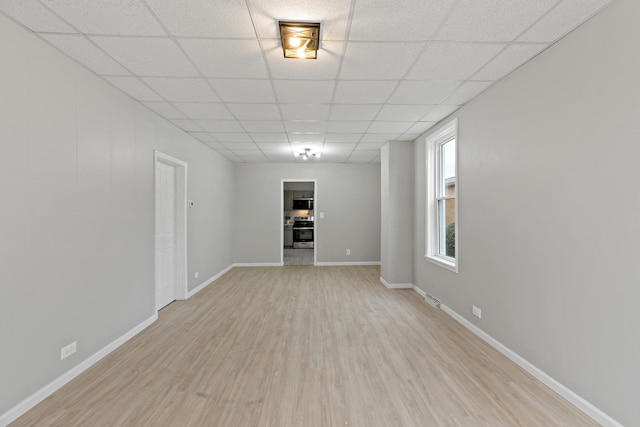 unfurnished living room with visible vents, baseboards, light wood finished floors, and a paneled ceiling