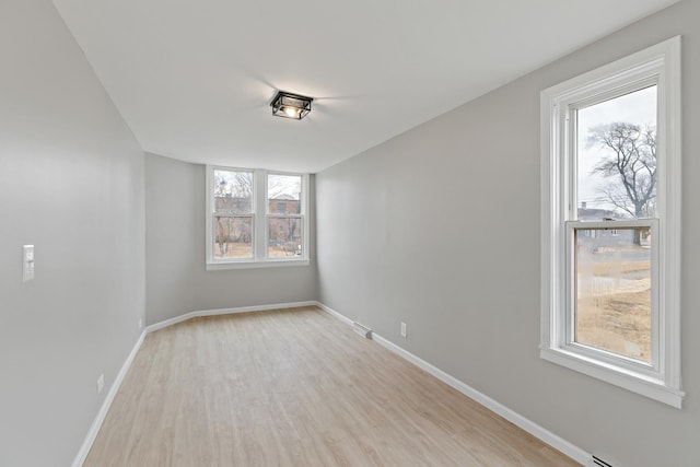 spare room featuring baseboards, a baseboard heating unit, and light wood-type flooring
