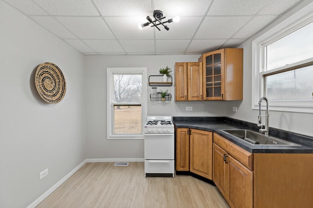 kitchen with white range with gas cooktop, light wood-style flooring, a sink, and brown cabinetry