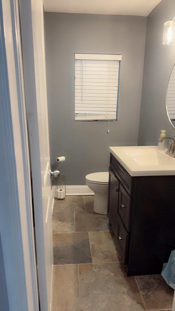8034 S Clyde Ave, Chicago, IL 60617 - half bathroom featuring baseboards, toilet, vanity, and stone tile floors