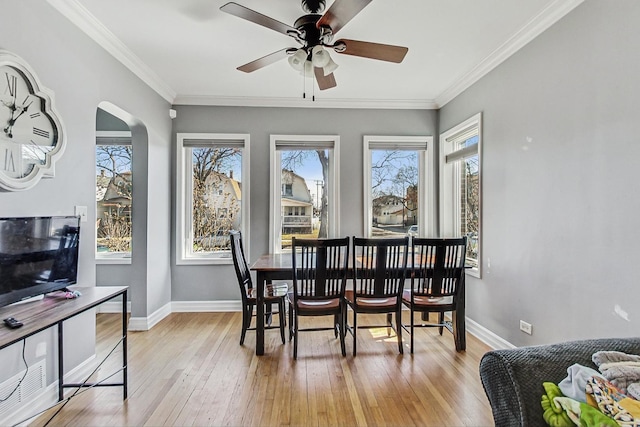 dining space featuring crown molding, baseboards, arched walkways, ceiling fan, and light wood-style flooring