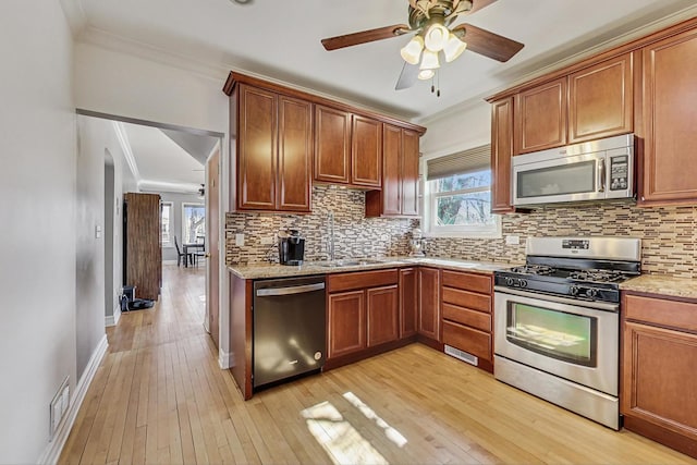 kitchen featuring crown molding, stainless steel appliances, a ceiling fan, a sink, and light wood-type flooring