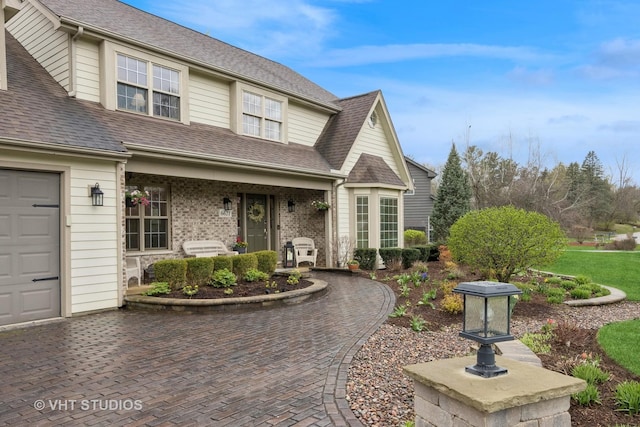 traditional-style house featuring roof with shingles, a garage, decorative driveway, and brick siding