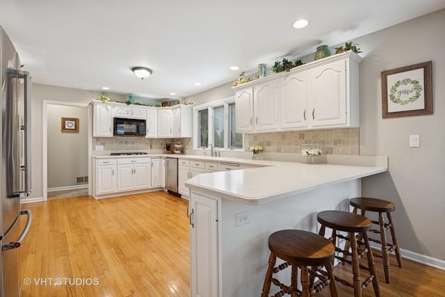 kitchen with a peninsula, a breakfast bar, white cabinets, backsplash, and black appliances