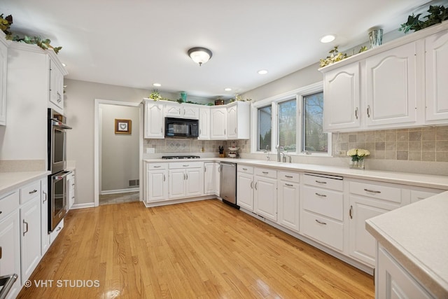kitchen featuring decorative backsplash, stainless steel appliances, light wood-style flooring, and white cabinets