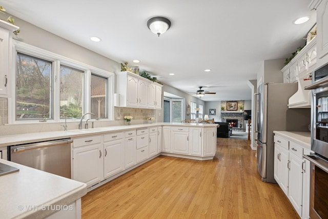 kitchen with white cabinets, appliances with stainless steel finishes, a sink, a stone fireplace, and backsplash