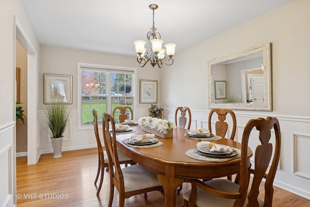 dining space with a wainscoted wall, light wood finished floors, and a chandelier