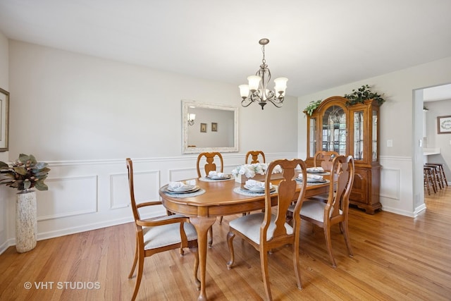 dining space featuring a decorative wall, a chandelier, wainscoting, and light wood-style floors
