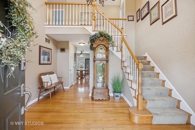 entryway featuring a towering ceiling, visible vents, wood finished floors, baseboards, and stairs