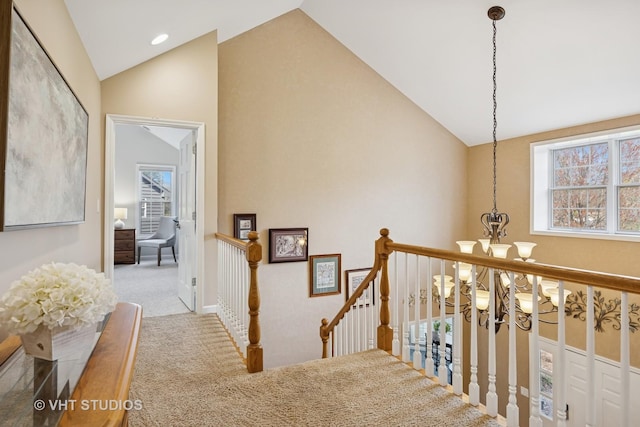 hallway featuring high vaulted ceiling, a chandelier, carpet, and an upstairs landing