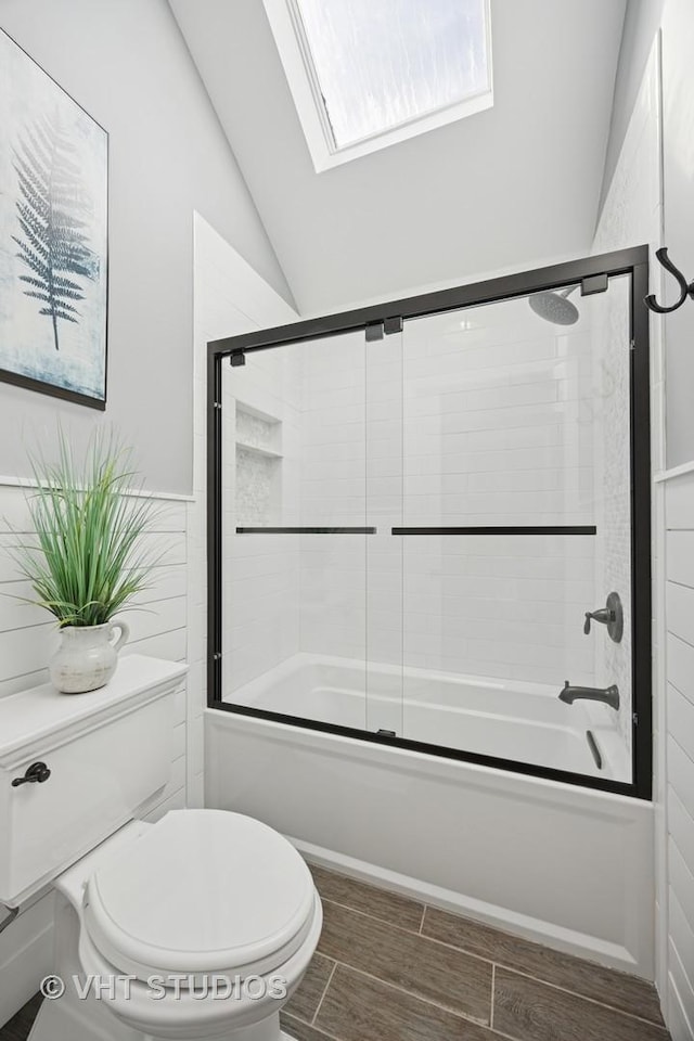 bathroom featuring a wealth of natural light, combined bath / shower with glass door, vaulted ceiling with skylight, and toilet