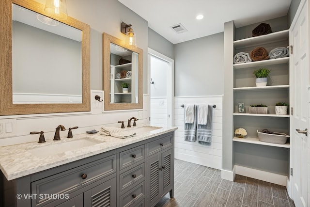 bathroom with double vanity, visible vents, a sink, and wood finished floors