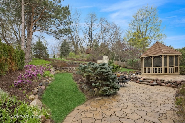 view of yard featuring fence, a patio, a shed, a gazebo, and an outbuilding
