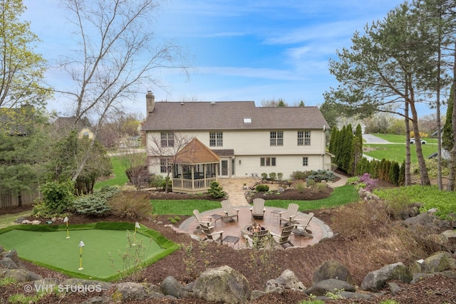 rear view of house featuring a patio, a fire pit, a sunroom, and a chimney