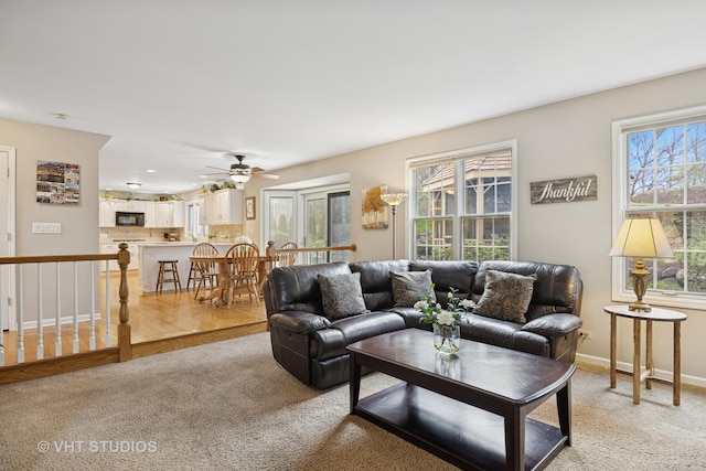living room featuring baseboards, light carpet, a ceiling fan, and a wealth of natural light