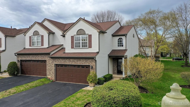 view of front of home featuring aphalt driveway, a shingled roof, a front yard, an attached garage, and brick siding