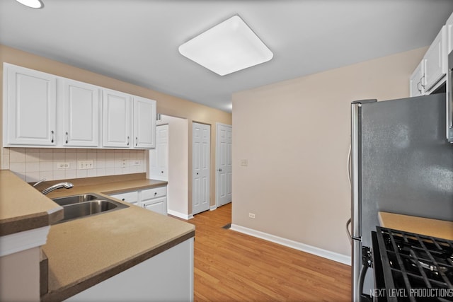 kitchen featuring a sink, decorative backsplash, light wood-style floors, white cabinets, and freestanding refrigerator