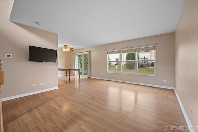 unfurnished living room with ceiling fan, baseboards, and light wood-type flooring
