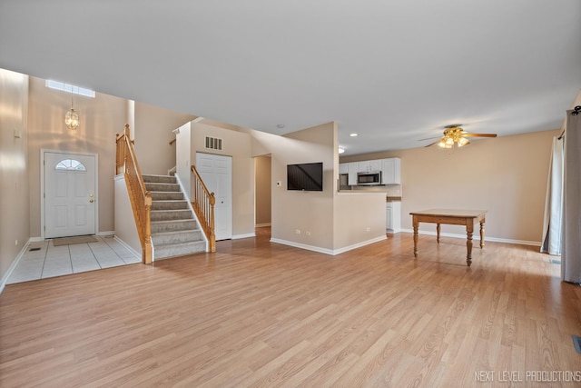 unfurnished living room featuring light wood finished floors, stairway, ceiling fan, visible vents, and baseboards