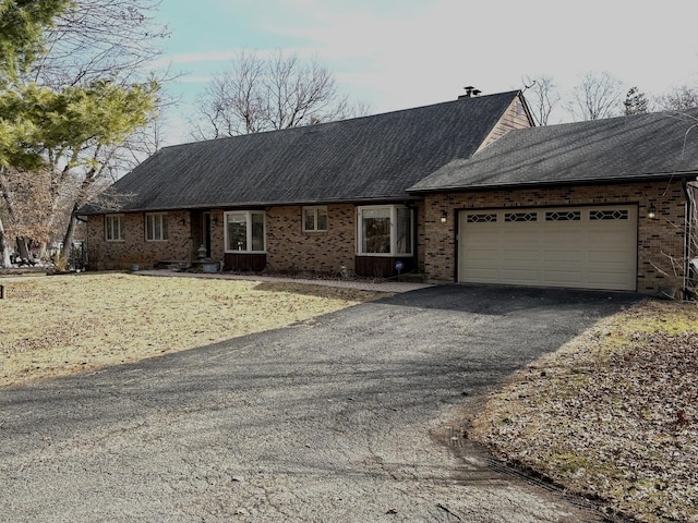 view of front of house featuring roof with shingles, an attached garage, driveway, brick siding, and a chimney