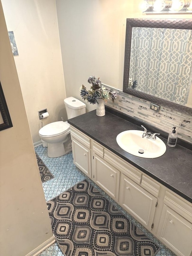 bathroom featuring tile patterned flooring, vanity, toilet, baseboards, and backsplash