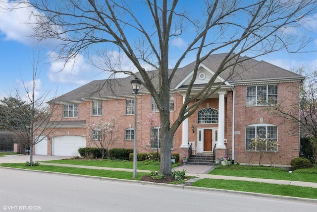 neoclassical / greek revival house featuring a front lawn, driveway, a garage, and brick siding