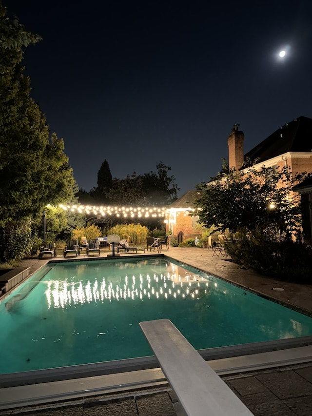 pool at twilight with a diving board, an outdoor pool, and a patio area
