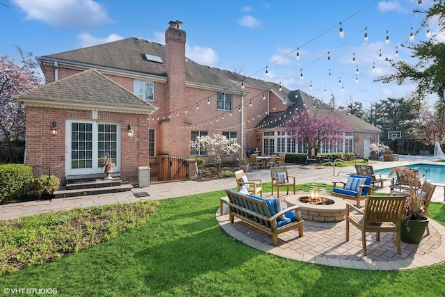 rear view of property with brick siding, a patio, an outdoor pool, and an outdoor fire pit