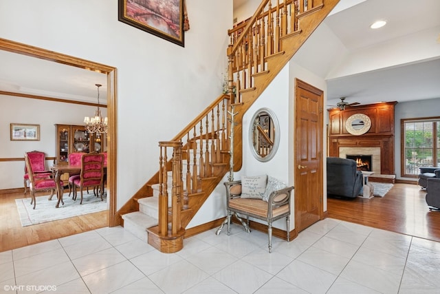 stairs with baseboards, a large fireplace, wood finished floors, and ceiling fan with notable chandelier