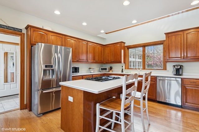 kitchen featuring a breakfast bar area, brown cabinets, appliances with stainless steel finishes, a kitchen island, and light countertops