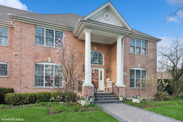 neoclassical home featuring a shingled roof and brick siding