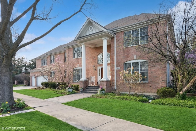 greek revival inspired property with brick siding, a front lawn, concrete driveway, and an attached garage