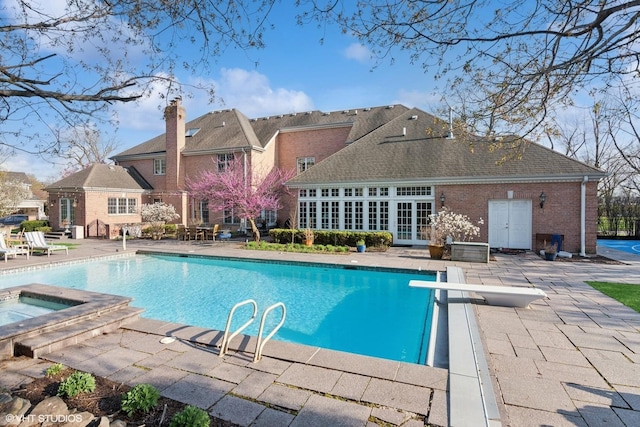 pool with a patio, a diving board, french doors, and an in ground hot tub