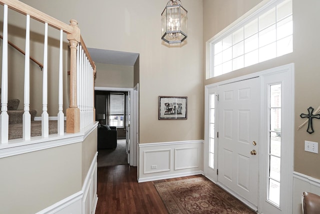 entryway featuring dark wood-type flooring, a wainscoted wall, a decorative wall, and a high ceiling