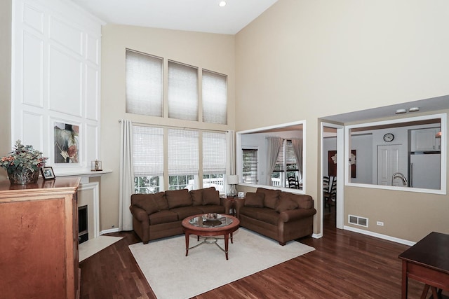 living room featuring dark wood-type flooring, high vaulted ceiling, visible vents, and a fireplace with flush hearth