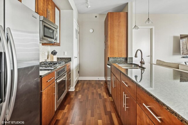 kitchen featuring stainless steel appliances, a sink, brown cabinets, dark wood-type flooring, and dark stone counters