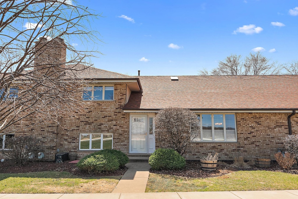view of front of home with brick siding, a chimney, and roof with shingles
