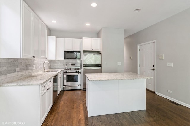 kitchen featuring stainless steel appliances, tasteful backsplash, a center island, a sink, and white cabinets
