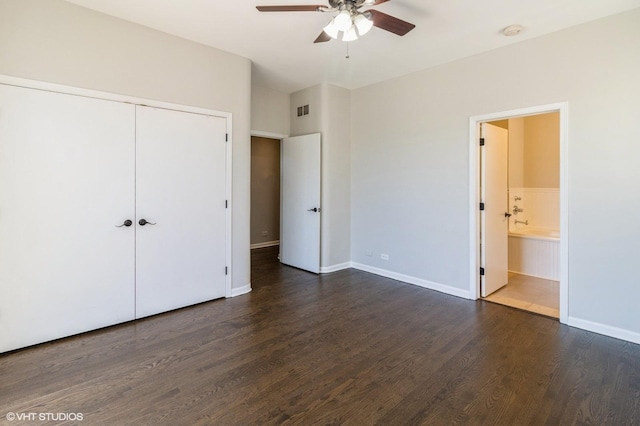 unfurnished bedroom featuring dark wood finished floors, a closet, baseboards, ensuite bath, and ceiling fan
