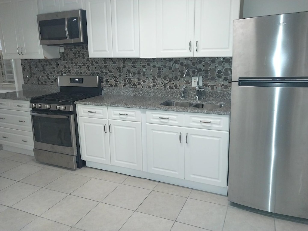 kitchen featuring stainless steel appliances, tasteful backsplash, white cabinetry, a sink, and light tile patterned floors