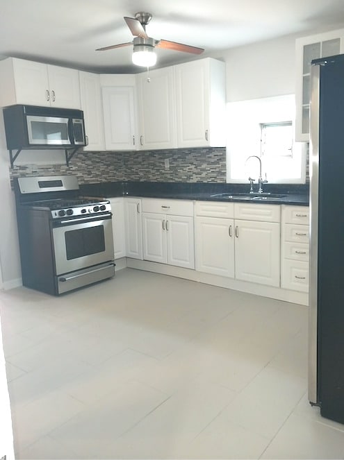 kitchen with tasteful backsplash, stainless steel appliances, a sink, dark countertops, and white cabinets