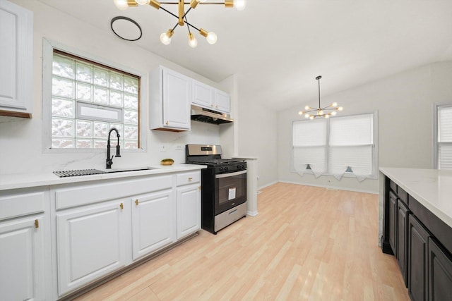 kitchen featuring light countertops, stainless steel gas stove, a sink, a chandelier, and under cabinet range hood