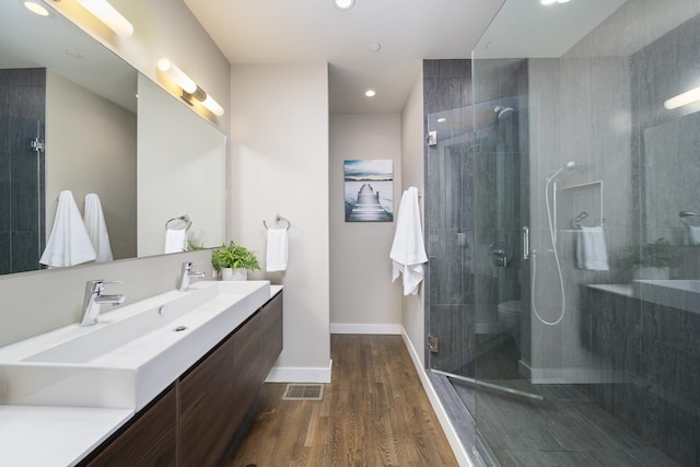 bathroom featuring tiled shower, wood finished floors, a sink, double vanity, and baseboards