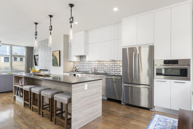 kitchen featuring backsplash, dark countertops, a kitchen island, dark wood-type flooring, and appliances with stainless steel finishes