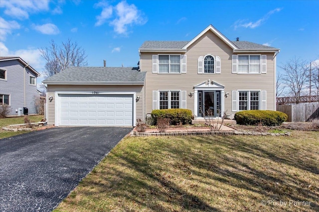 colonial home featuring aphalt driveway, fence, a garage, a front yard, and roof with shingles